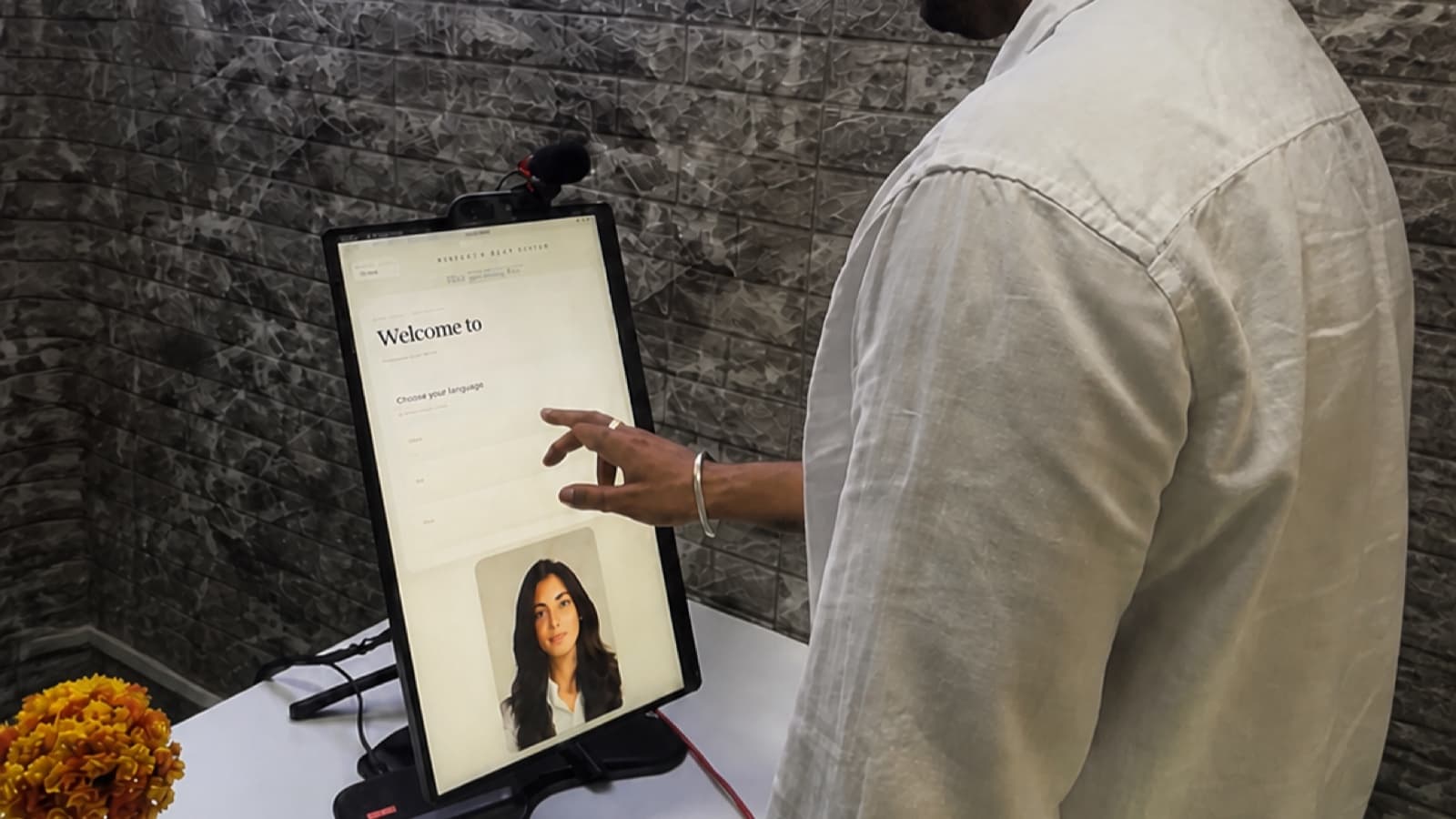 The Aagman kiosk on a reception counter at the pilot site, showing the welcome and language-selection screen.
